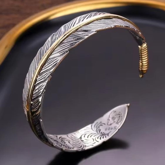 Adjustable feather cuff bracelet in silver tone with a gold-tone line along the quill