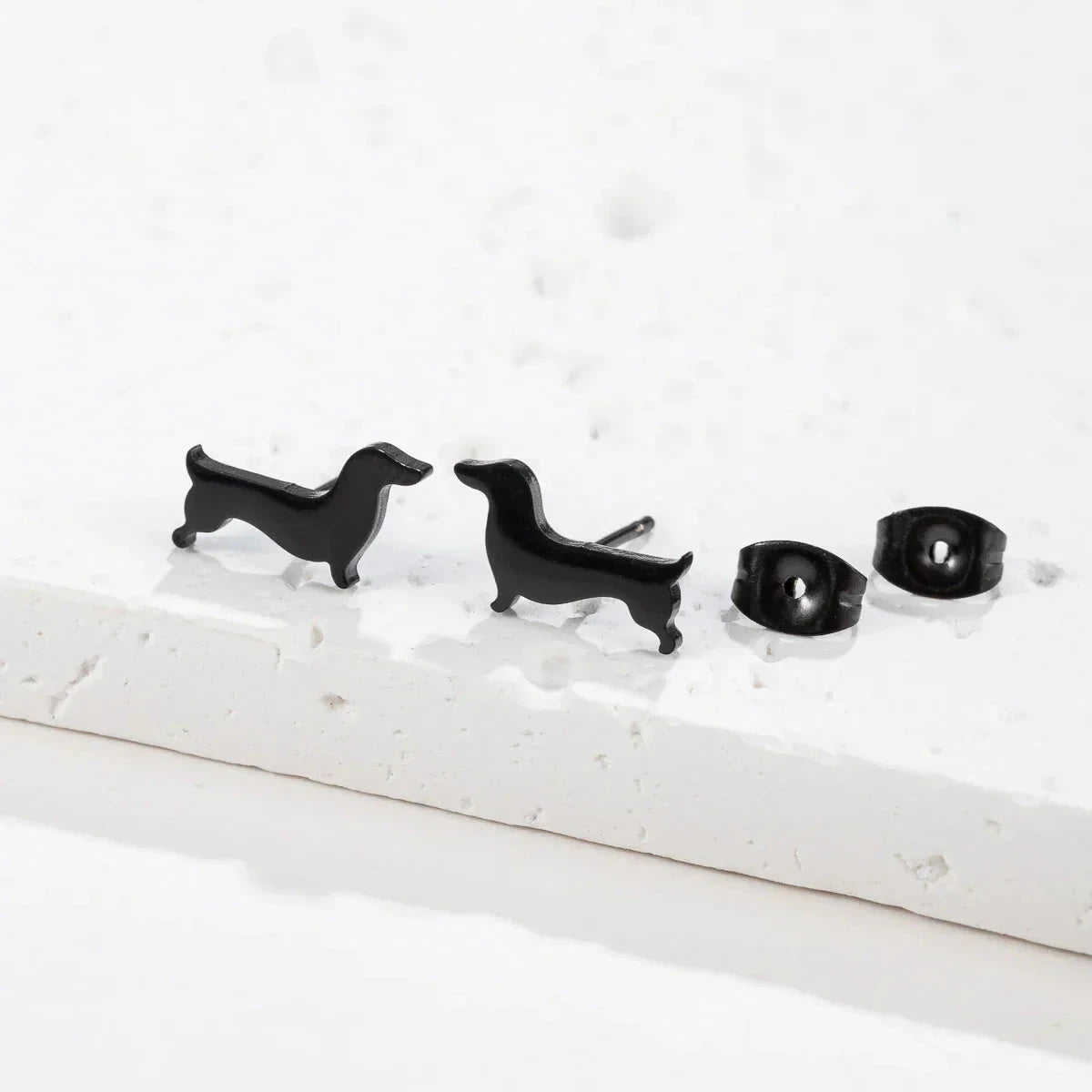Black dachshund stud earrings on a stone slab with their butterfly backs