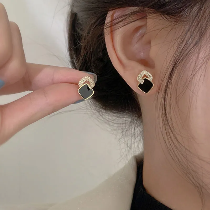 Black square stud earring in gold tone with a crystal-set arch, worn on the ear