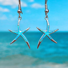 Blue opal starfish drop earrings in silver tone, photographed against the sea