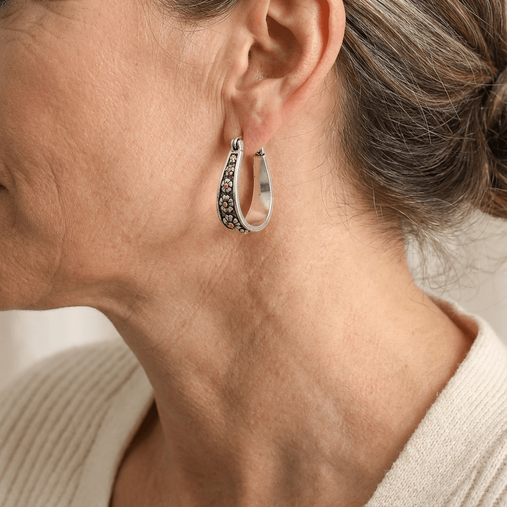 Brushed silver-tone oval hoop earrings with small gold-tone daisy motifs