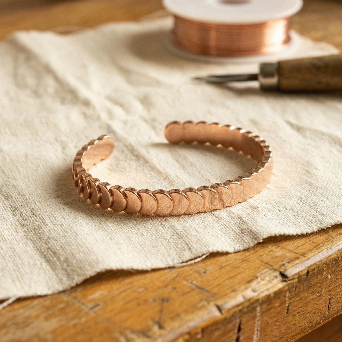 Copper cuff bracelet made of small overlapping discs, resting on a linen cloth