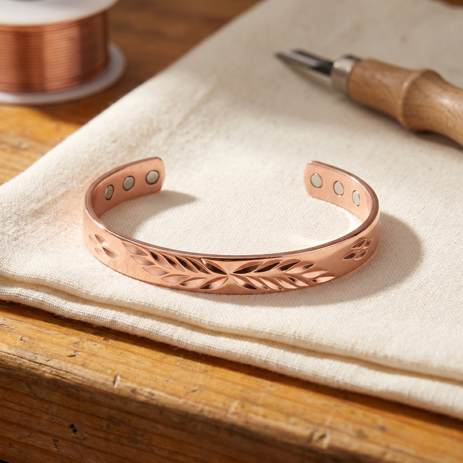 Copper-tone open cuff bracelet with a carved leaf pattern along the band and inset discs at each end
