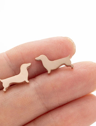 Dachshund stud earrings in copper tone resting on fingers