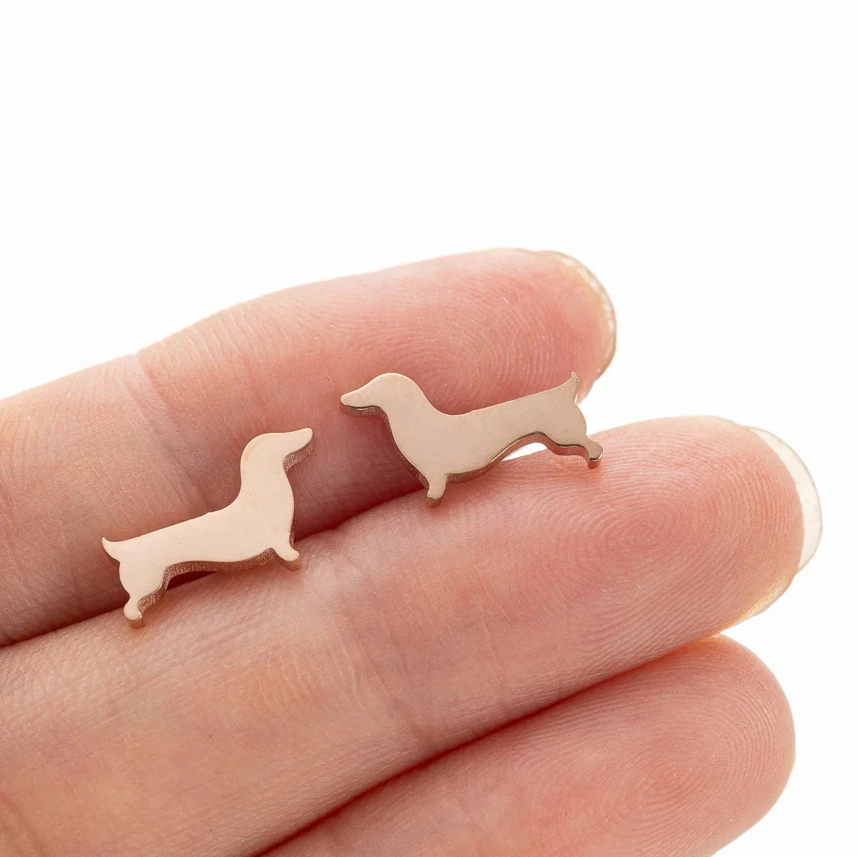 Dachshund stud earrings in copper tone resting on fingers