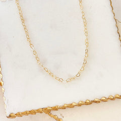 Fine gold-tone heart chain necklace laid out on a marble tray