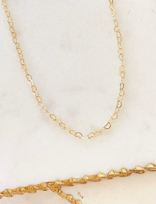Fine gold-tone heart chain necklace laid out on a marble tray