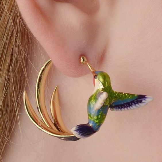 Gold-tone hummingbird hoop earring with green and blue enamel worn on the ear