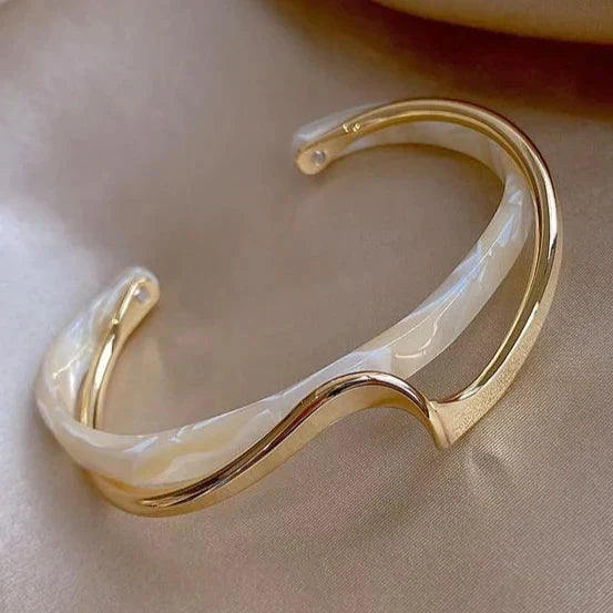 Gold-tone open cuff bracelet with a polished wave of metal across a pearl-white marbled inlay