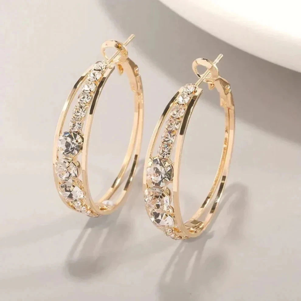 Gold-tone oval hoop earrings with a row of graduated clear crystals set into a groove along the front