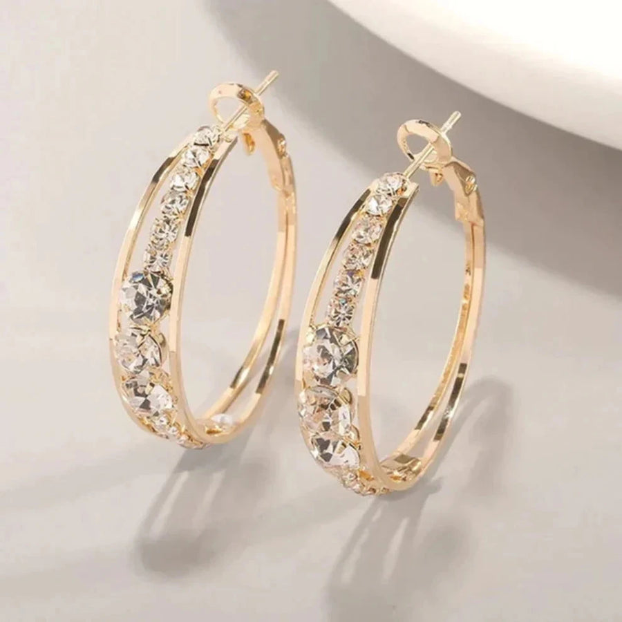 Gold-tone oval hoop earrings with a row of graduated clear crystals set into a groove along the front