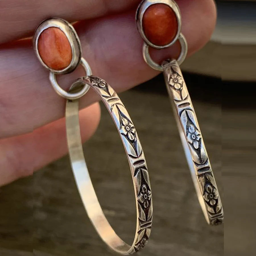 Large silver-tone hoop earrings with a stamped pattern hanging from an oval red-orange stone stud