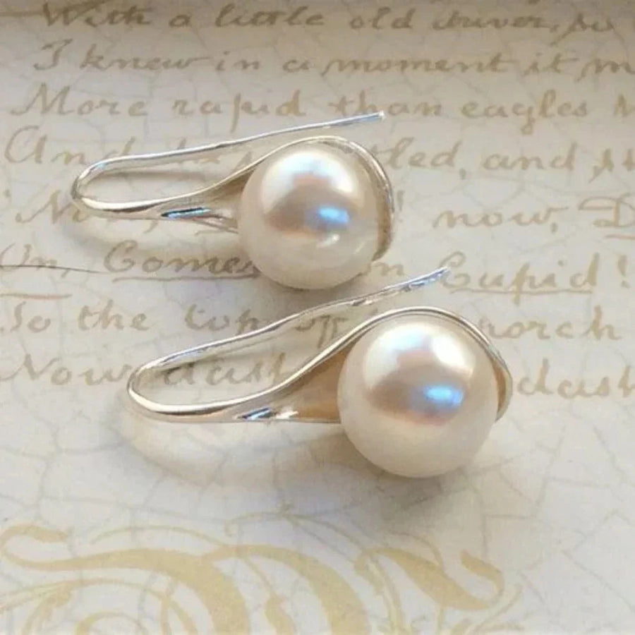 Pair of pearl drop earrings with round cream pearls held in curved polished silver-tone hook wires