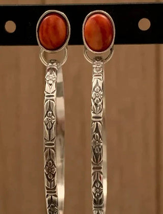 Pair of stamped silver-tone hoop earrings with red-orange oval stones on a display card