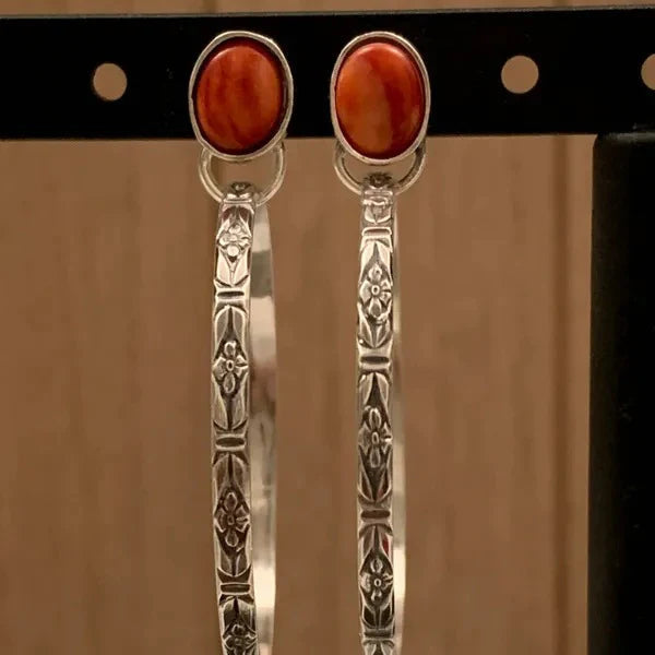Pair of stamped silver-tone hoop earrings with red-orange oval stones on a display card