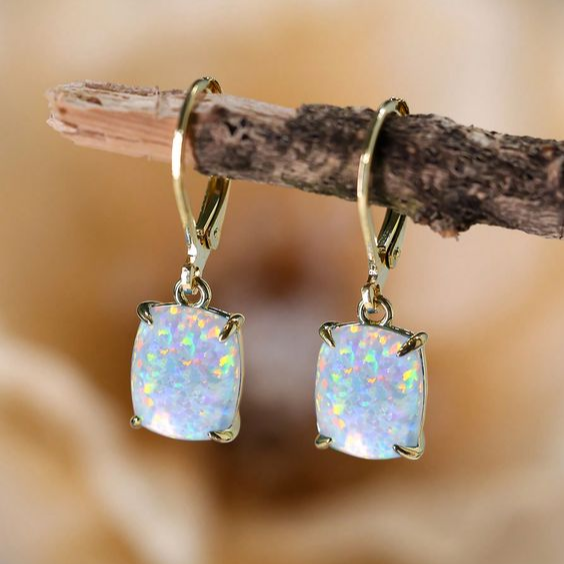 Pair of white opal drop earrings in gold-tone claw settings on leverback hooks, hanging from a branch