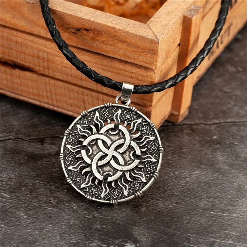 Round silver-tone talisman pendant with a four-way knot inside a carved sun, on a braided black cord