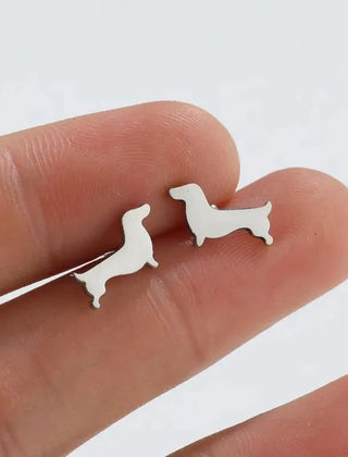 Silver-tone dachshund stud earrings held on a fingertip to show their size