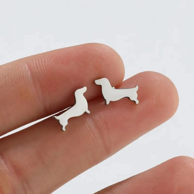 Silver-tone dachshund stud earrings held on a fingertip to show their size