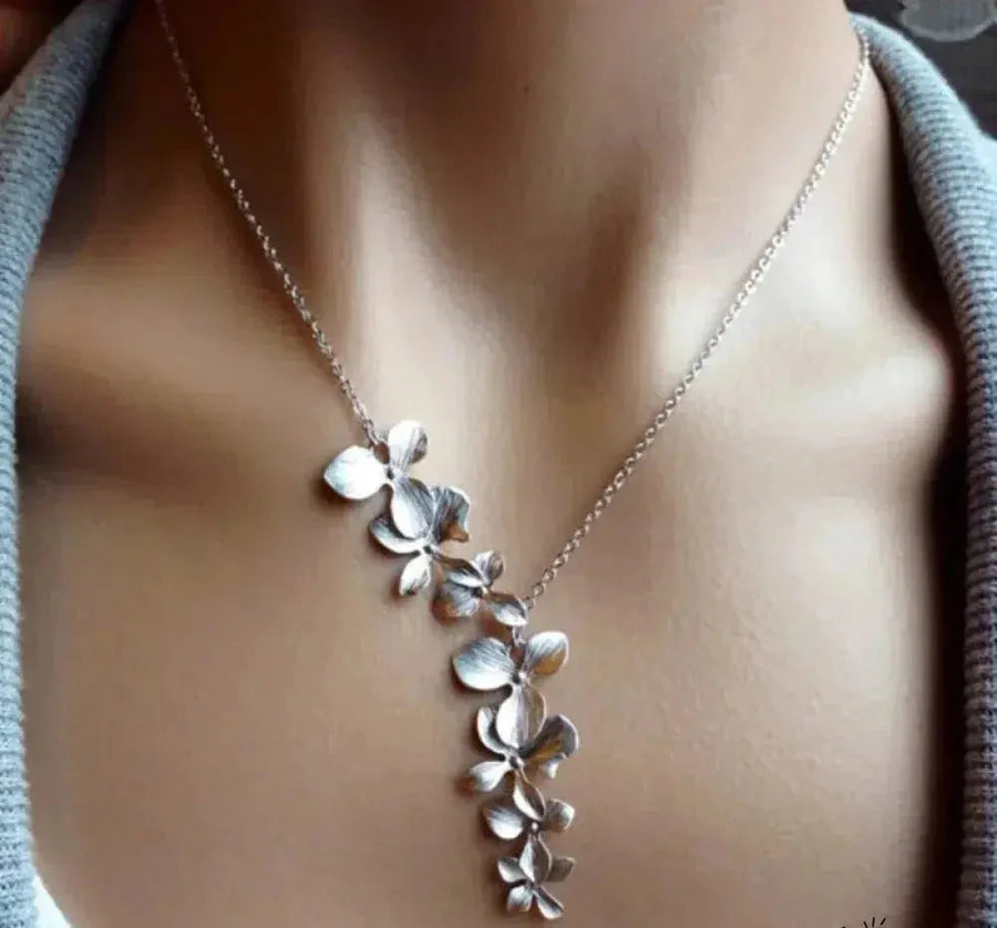Silver-tone flower necklace with five orchid blooms cascading down one side, worn with a grey knit