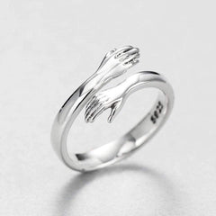 Silver-tone hug ring with two sculpted arms and open hands wrapping around the band