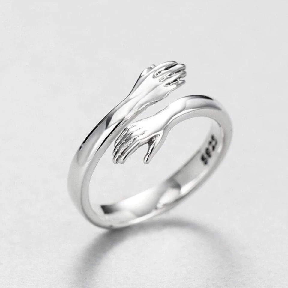 Silver-tone hug ring with two sculpted arms and open hands wrapping around the band