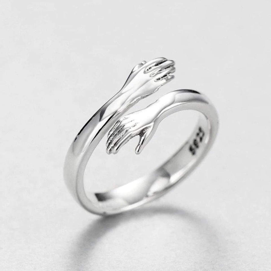 Silver-tone hug ring with two sculpted arms and open hands wrapping around the band