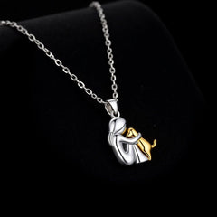 Silver-tone pendant of a seated figure hugging a gold-tone dog, on a fine chain
