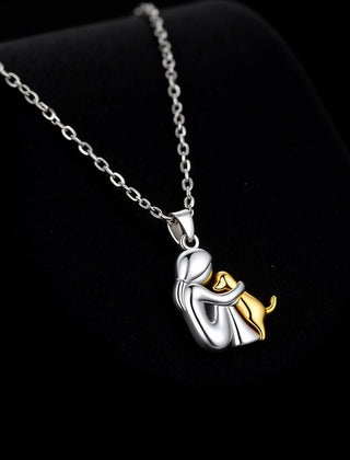 Silver-tone pendant of a seated figure hugging a gold-tone dog, on a fine chain