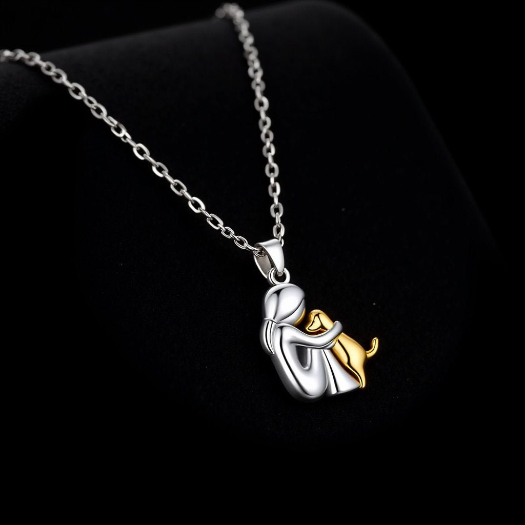 Silver-tone pendant of a seated figure hugging a gold-tone dog, on a fine chain