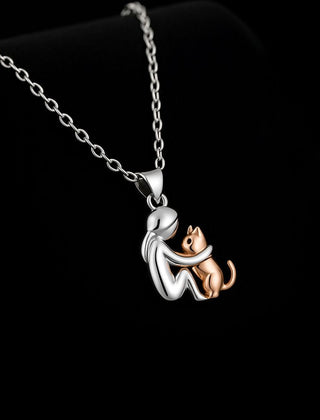 Silver-tone pendant of a seated figure hugging a rose gold-tone cat, on a fine cable chain
