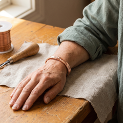 The copper cuff bracelet worn on a wrist, showing how it sits under a rolled sleeve