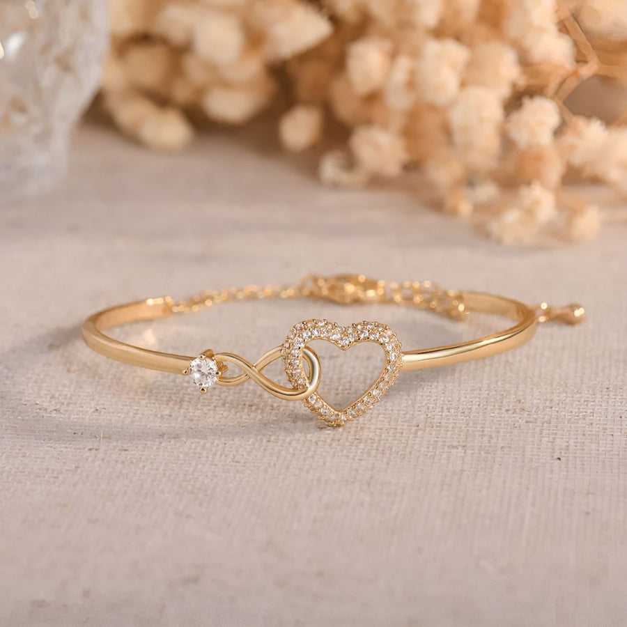The gold-tone infinity heart bangle photographed beside dried flowers