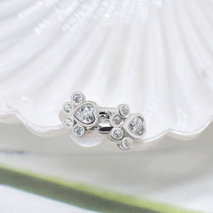 The paw huggie earrings resting together in a white shell dish