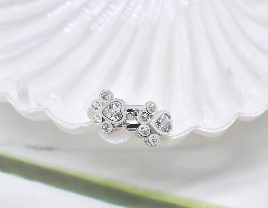 The paw huggie earrings resting together in a white shell dish