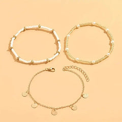 Three gold-tone anklets laid out flat: white beaded, double beaded and a disc chain
