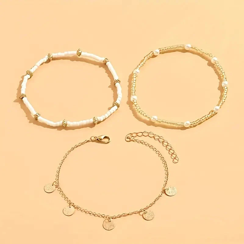 Three gold-tone anklets laid out flat: white beaded, double beaded and a disc chain