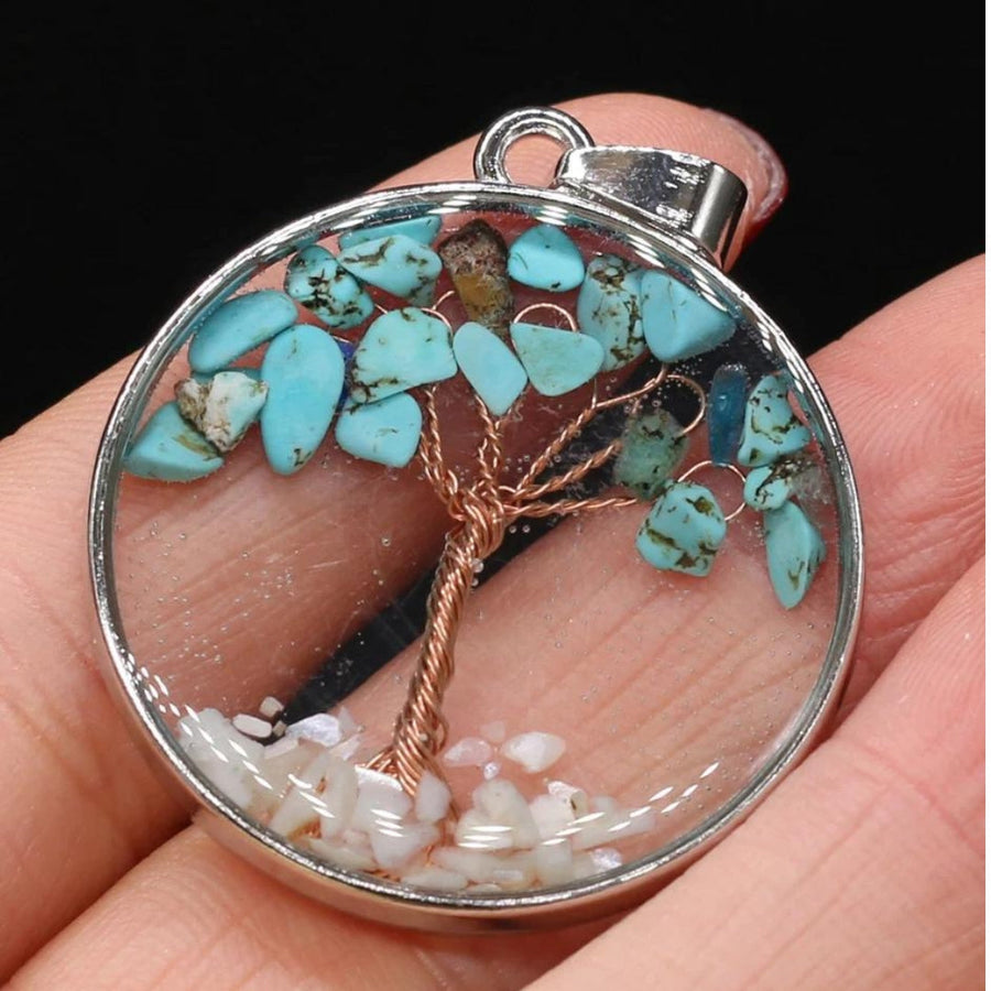 Tree of life pendant with a copper-tone wire tree and turquoise-blue stone chips behind clear glass in a round silver-tone frame
