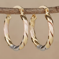 Twisted hoop earrings in gold, rose gold and silver tone hanging from a branch