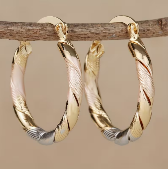 Twisted hoop earrings in gold, rose gold and silver tone hanging from a branch