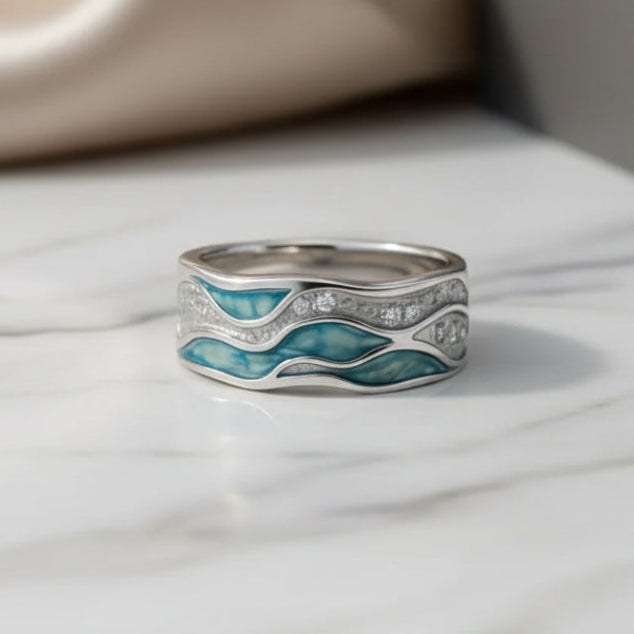 Wide silver-tone ring with turquoise wave inlay and sparkling bands, on a marble surface